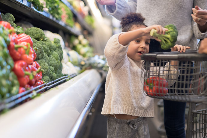 A young child places broccoli into a shopping trolley