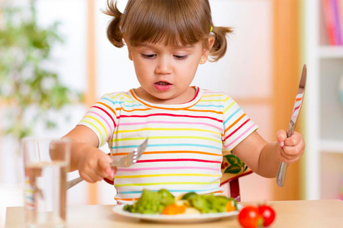 A child holding a knife and fork, about to eat a plate of vegetables
